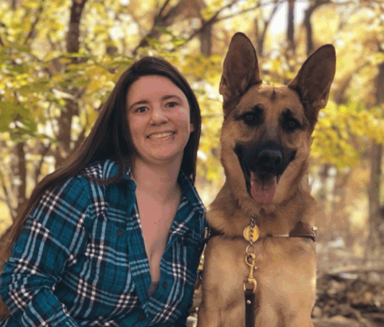 Photo of Meagan Gorsuch and her German Shepherd Dog, Henna sitting outdoors in the autumn trees